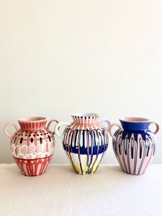 three colorful vases sitting on top of a white table next to eachother