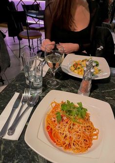 a woman sitting at a table with two plates of spaghetti and wine glasses on it