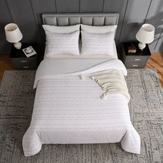 a bed with white sheets and pillows in a bedroom next to two nightstands on either side of the bed