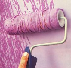 a person using a paint roller to paint a wall with pink and purple streaks on it