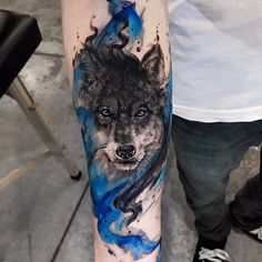 a man's arm with a wolf tattoo on it and blue watercolors