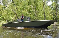 a man sitting on the back of a green boat in a river surrounded by trees