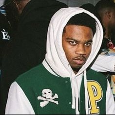 a man wearing a green and white hoodie with a skull on the side, standing in front of other people