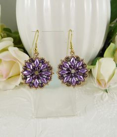 a pair of purple earrings sitting on top of a white table next to some flowers