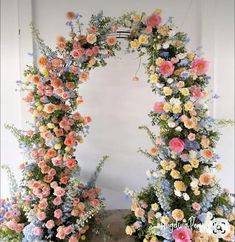 an arch made out of flowers and greenery with blue, pink, yellow and white flowers