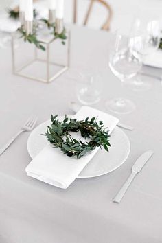 the table is set with white plates, silverware and greenery wreaths on them