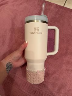 a person holding a white travel mug with a straw in it on a pink blanket