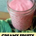 a jar filled with pink liquid sitting on top of a green leafy tablecloth