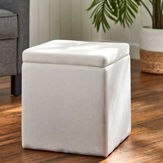 a white storage box sitting on top of a wooden floor next to a chair and potted plant