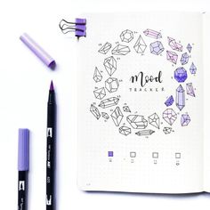 an open notebook with markers and pens on it, next to a pen that says mood tracker