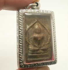 a hand holding a silver square pendant with a design on the front and back side