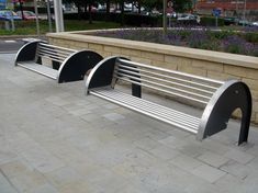 three metal benches sitting next to each other on a brick walkway near a flower garden