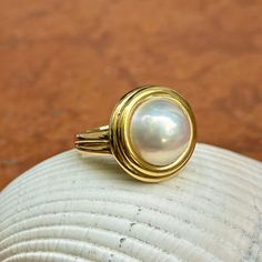 New, but old pieces, never worn, recently acquired from a premiere jeweler located in Minneapolis, MN for many years- a rare opportunity. 18KT yellow gold genuine, double bezel, round, mabe pearl ring Size 6.50 Sizable by us for a fee or your local jeweler Weight: 12.2 grams Band width: 3mm in back 11.50~12mm round mabe pearl Stamped 18k Anniversary Yellow Gold Pearl Ring With Cabochon, Luxury Yellow Gold Pearl Ring With Cabochon, Classic Gold Rings With High Luster, Classic Gold Pearl Ring With Polished Finish, Heirloom Pearl Ring With Polished Finish, Gold Rings With High Luster, Classic White Pearl Ring With Bezel Setting, Classic Cabochon Pearl Ring For Formal Occasions, Classic Round Pearl Ring With High Luster