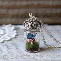 a tiny glass jar filled with moss and a blue butterfly