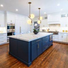 a large kitchen with white cabinets and blue island in the center is surrounded by wood flooring