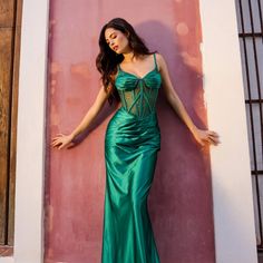 a woman in a long green dress leaning against a wall with her hands on her hips