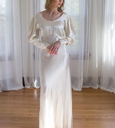 a woman standing in front of a window wearing a white dress with puffy sleeves