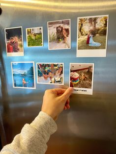 a person holding up pictures on the side of a refrigerator with magnets attached to it