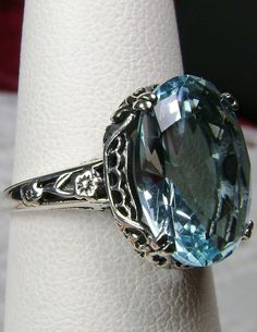 Simulated Aquamarine Ring Edward Design#70 Custom Made Here we have an Edwardian reproduction ring in sterling silver filigree with a perfect Simulated/Man-made blue aquamarine gemstone solitaire. This full cut oval gem is 14mm in length and 10mm in width (slightly smaller gemstone also available upon request). This ring also sits 7mm off the finger. The inside of the band is marked 925 for solid sterling. Notice the beautiful leaf design of the silver filigree setting and etched band. This is a Oval Aquamarine Jewelry For Wedding, Oval Aquamarine Wedding Jewelry, Exquisite Aquamarine Wedding Jewelry, Classic Vs Clarity Topaz Jewelry, Classic Oval Aquamarine Jewelry, Elegant Oval Sapphire Ring With Vs Clarity, Victorian Topaz Jewelry For Formal Occasions, Classic Aquamarine Jewelry For Anniversary, Hallmarked Aquamarine Jewelry For Anniversary