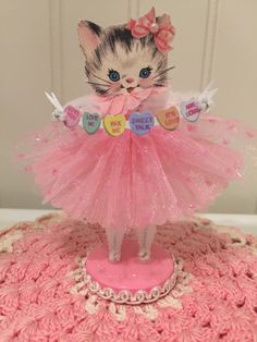 a cat figurine in a pink dress on top of a doily