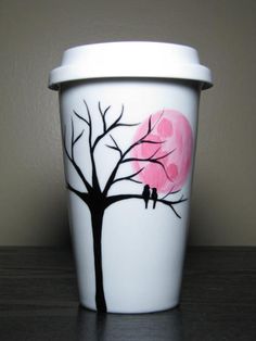 a coffee cup with a tree painted on the side and a pink moon behind it