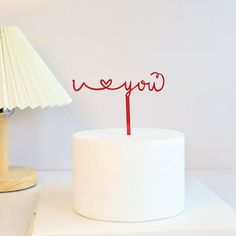 a white cake with a red name on it and a lamp next to the cake