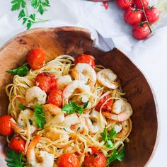 pasta with shrimp, tomatoes and parsley in a wooden bowl on a white table