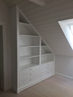 an attic bedroom with white shelves and drawers