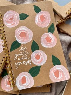 notebooks with painted flowers on them and the words be gentle until yourself written in white ink