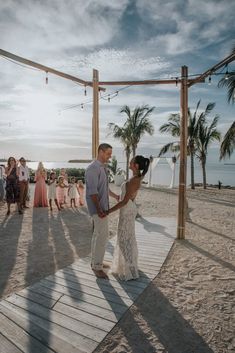 a bride and groom dance on the beach at their wedding reception in front of palm trees