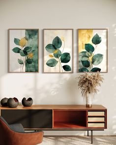 three paintings hang on the wall next to a chair and vase with plants in it