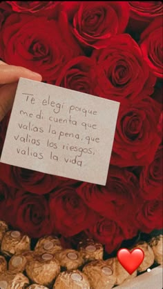 a person holding a card in front of a bunch of red roses and some cookies