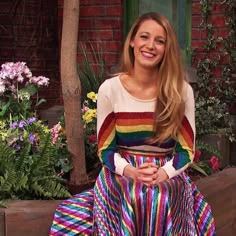 a woman sitting on a bench wearing a colorful dress and smiling at the camera with her hands folded