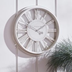 a clock hanging on the side of a white wall next to a potted plant