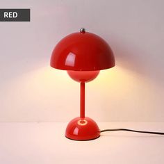 a red table lamp sitting on top of a white counter next to a light bulb