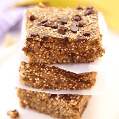 three granola bars stacked on top of each other with chocolate chips and bananas in the background