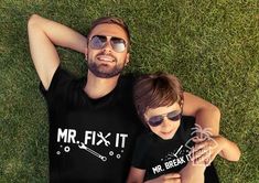 a man and boy laying on the grass with their arms around each other wearing matching t - shirts