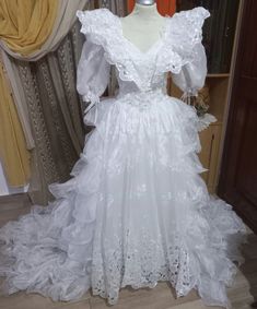 a white wedding dress on display in front of a window with curtains and drapes