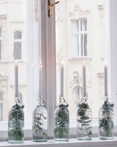 three glass bottles with plants in them sitting on a window sill next to candles