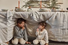 two children sitting on the floor in front of a table covered with white cloths