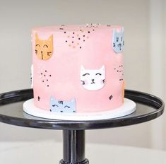 a pink cake with cats on it sitting on top of a black stand in front of a white wall