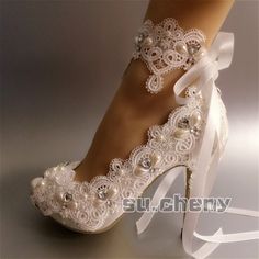 a woman's white high heeled shoes with pearls and bows