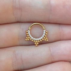 a small gold nose ring with white stones on the top and bottom, sitting in someone's hand