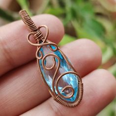 a hand holding a wire wrapped pendant with a blue topazte stone in it