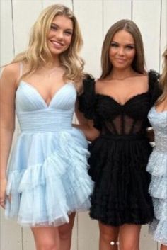 three beautiful women standing next to each other in front of a white wall wearing dresses