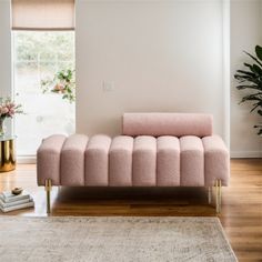 a pink couch sitting on top of a wooden floor next to a plant in a living room