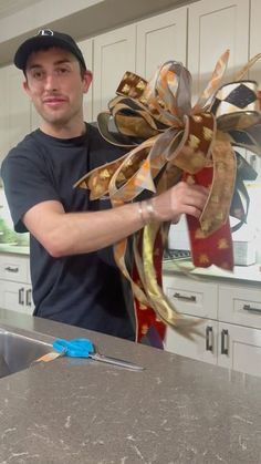 a man standing in front of a kitchen counter holding onto a large bow with scissors next to it