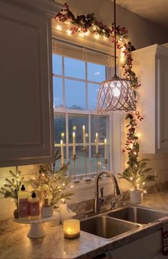 a kitchen sink under a window with christmas lights hanging from it's side and candles on the windowsill