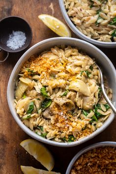 two bowls filled with pasta and spinach on top of a wooden table next to lemon wedges