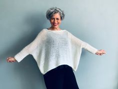 an older woman standing in front of a blue wall with her arms spread out and smiling